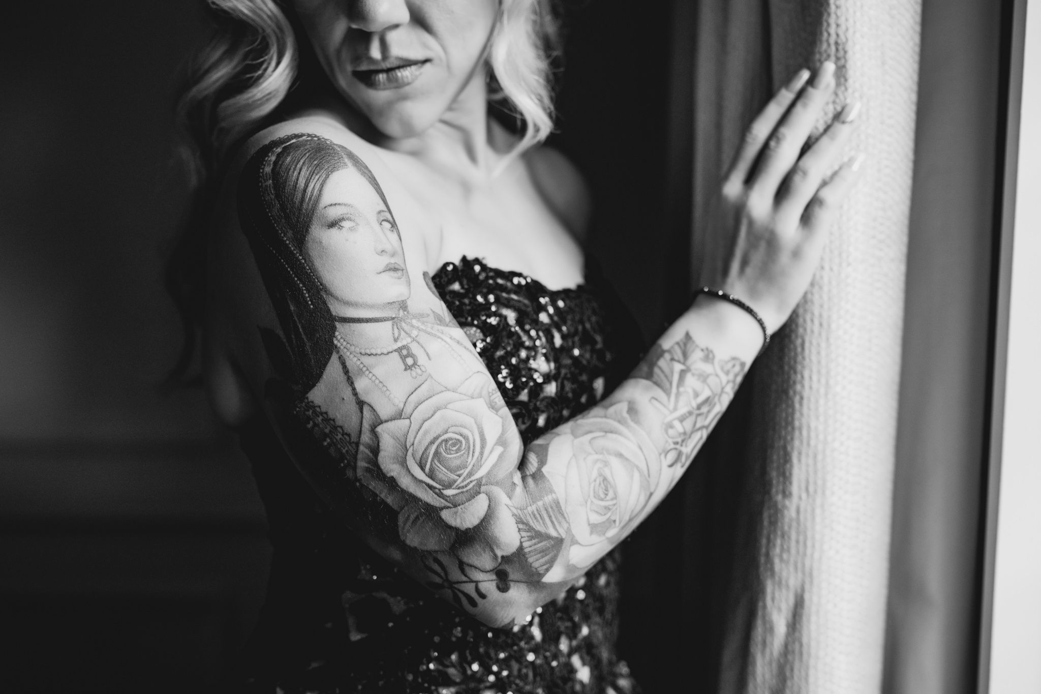 Close-up details of tattooed arms and wedding dress in dramatic window light.