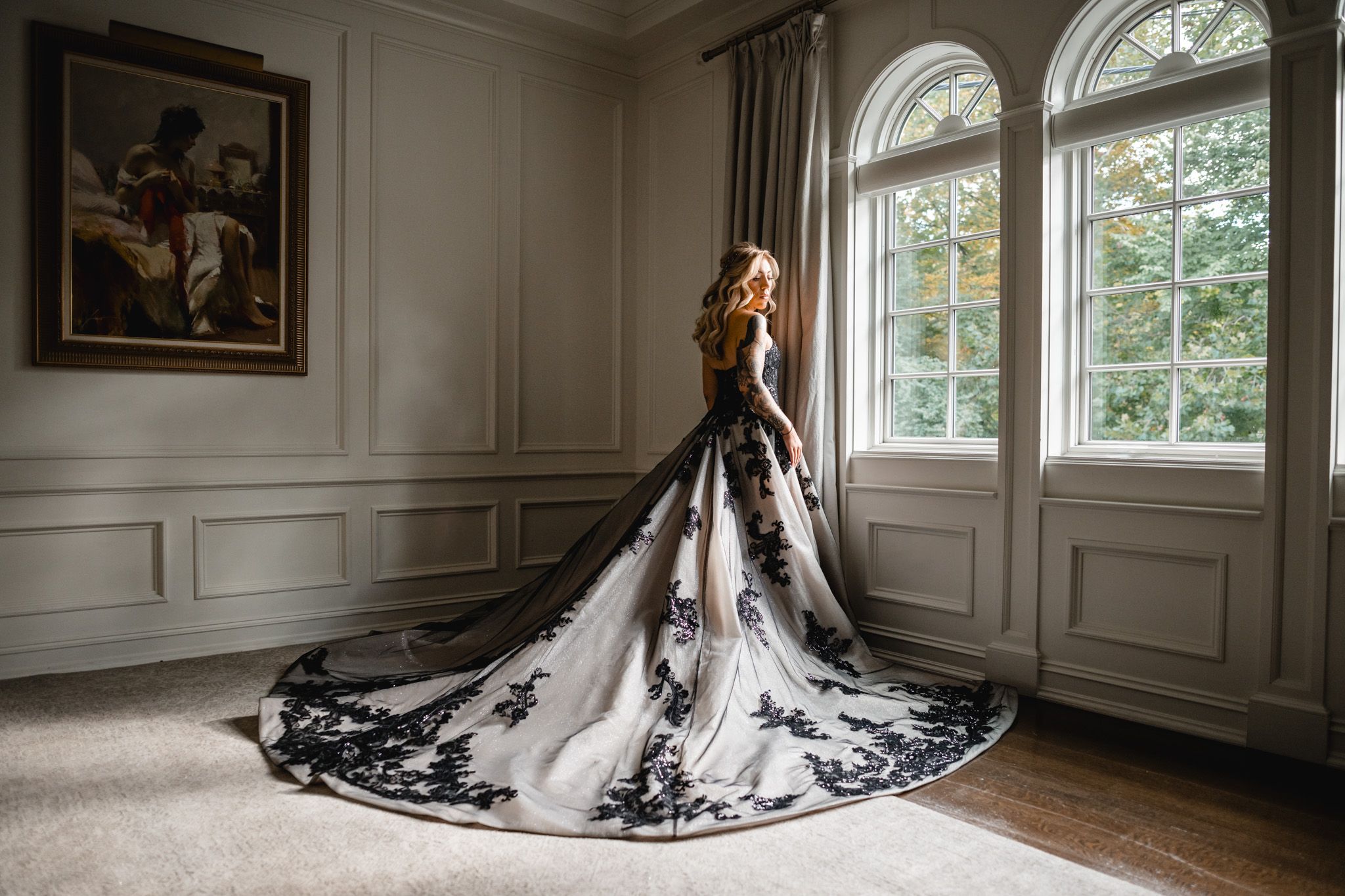 A stunning black and white wedding dress with lace details fills an elegant room with arched windows and wainscoting.
