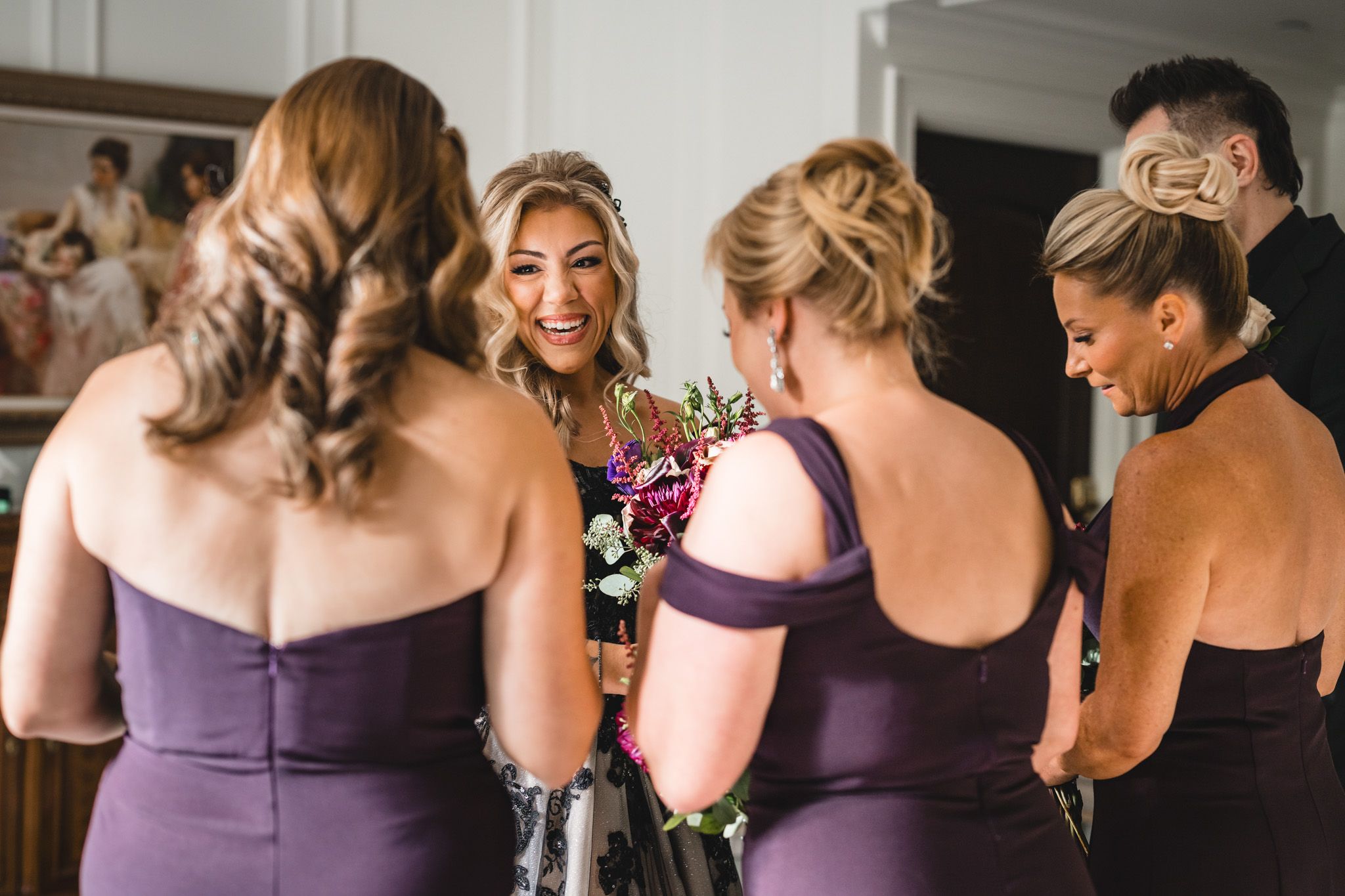 Group wearing purple bridesmaid dresses gathered in conversation during wedding preparations.