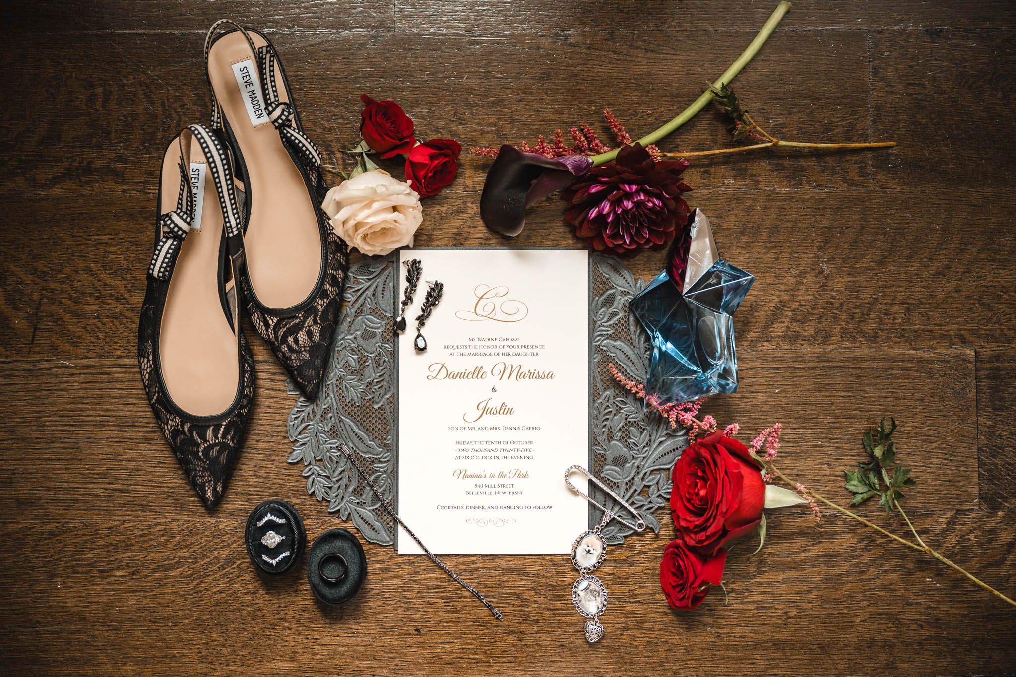 Wedding details with red roses, invitation and elegant black shoes on rustic wooden surface.