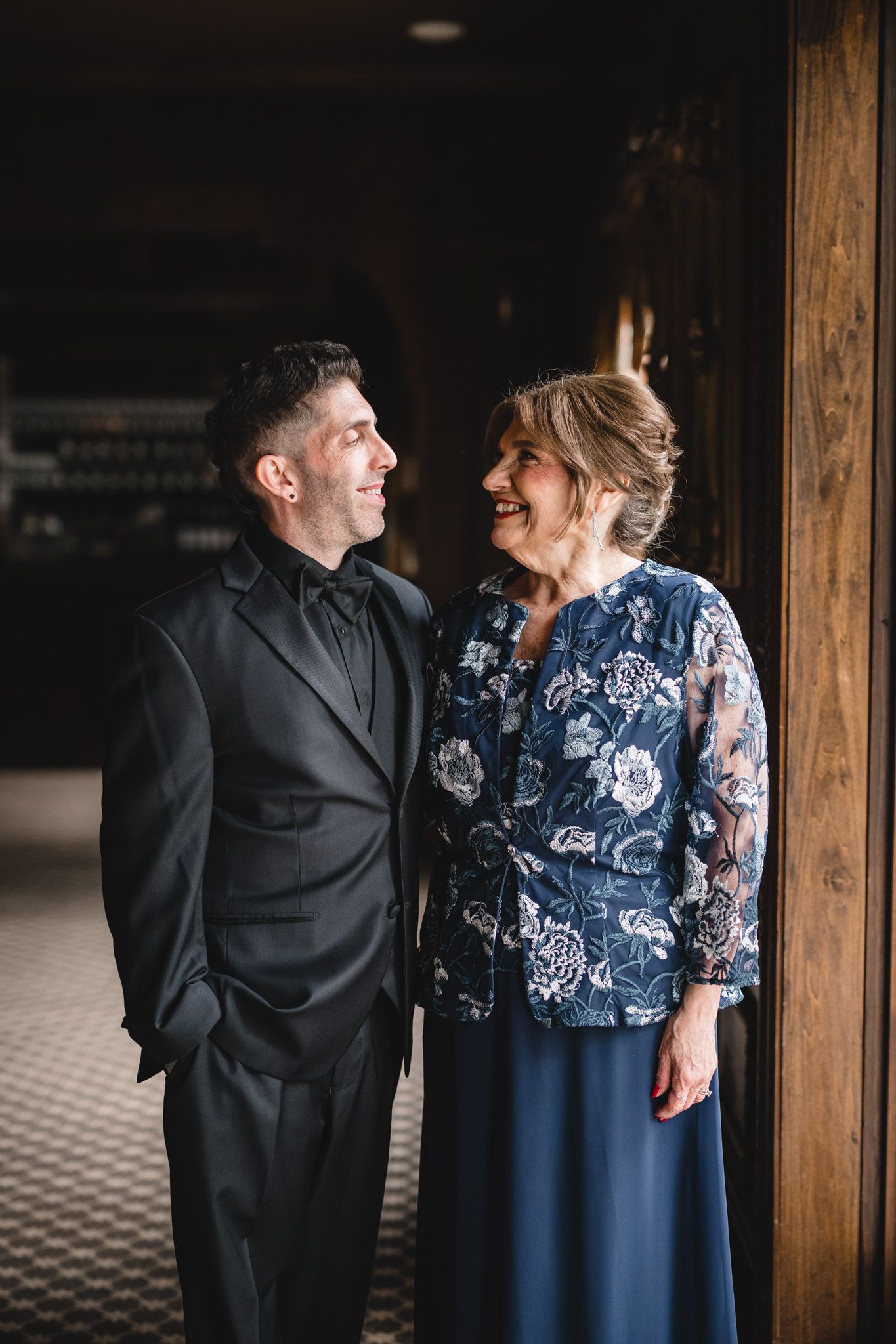 Couple in formal attire sharing an intimate moment near wooden pillars indoors.