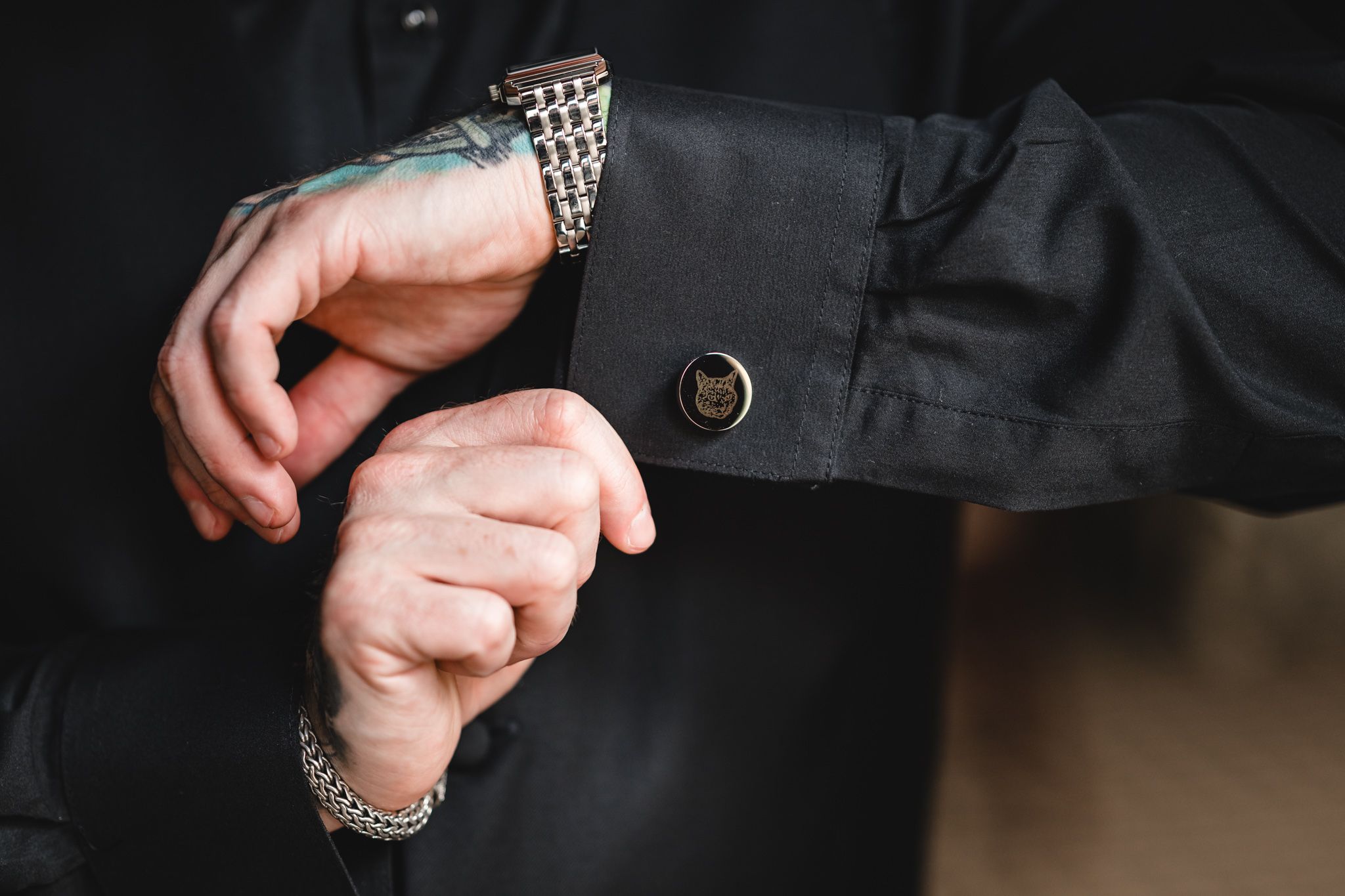 Close-up detail of hands adjusting a black suit jacket sleeve in a dimly lit room.