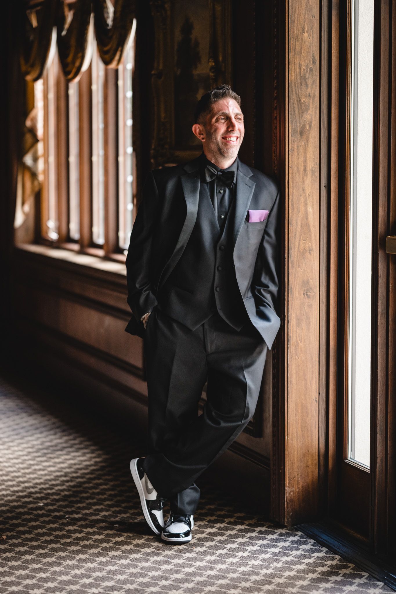 Person in black suit sitting by wooden window frames with checkered floor pattern.