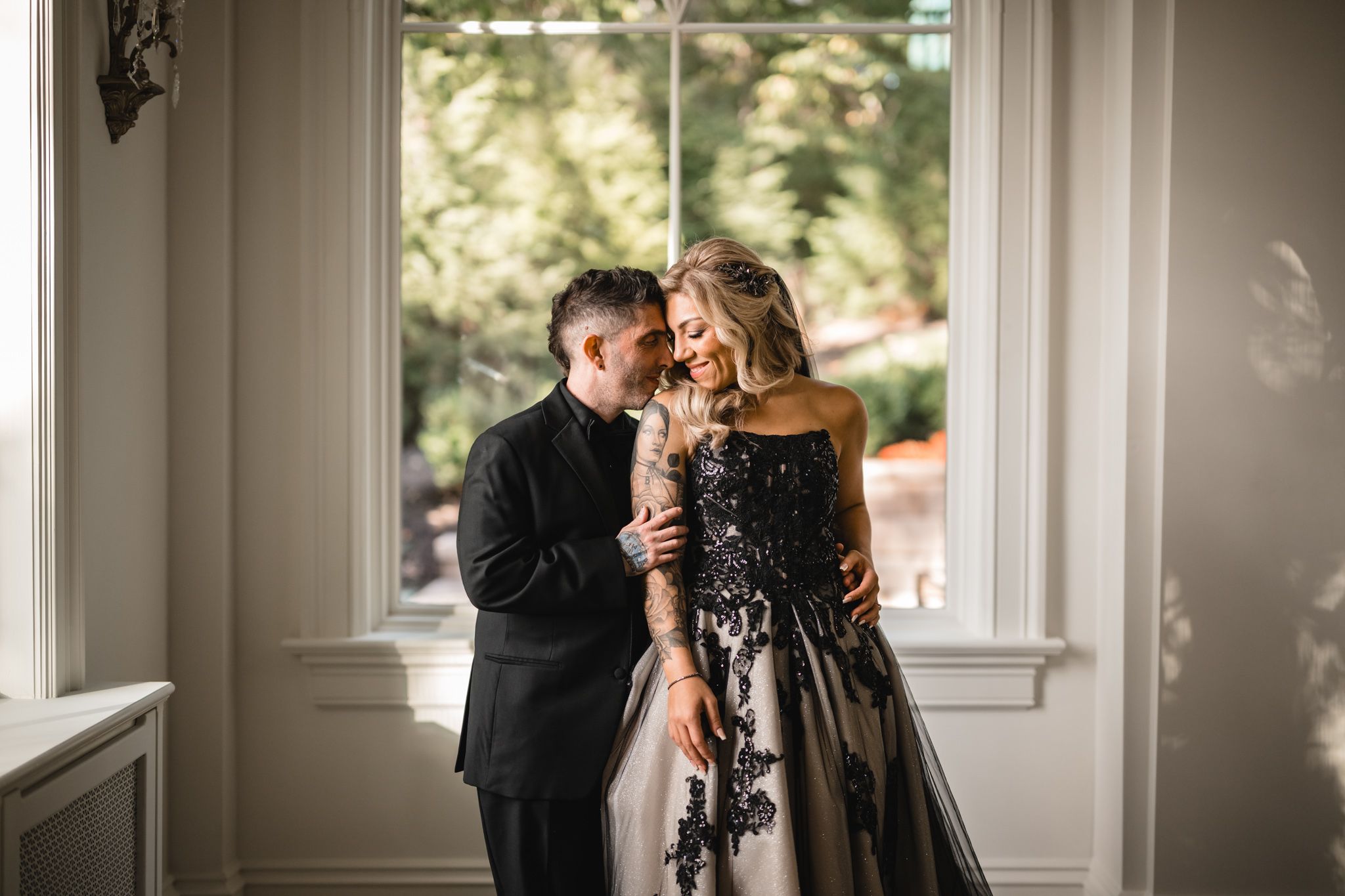 A romantic moment captured between a couple in formal attire by a bright window.