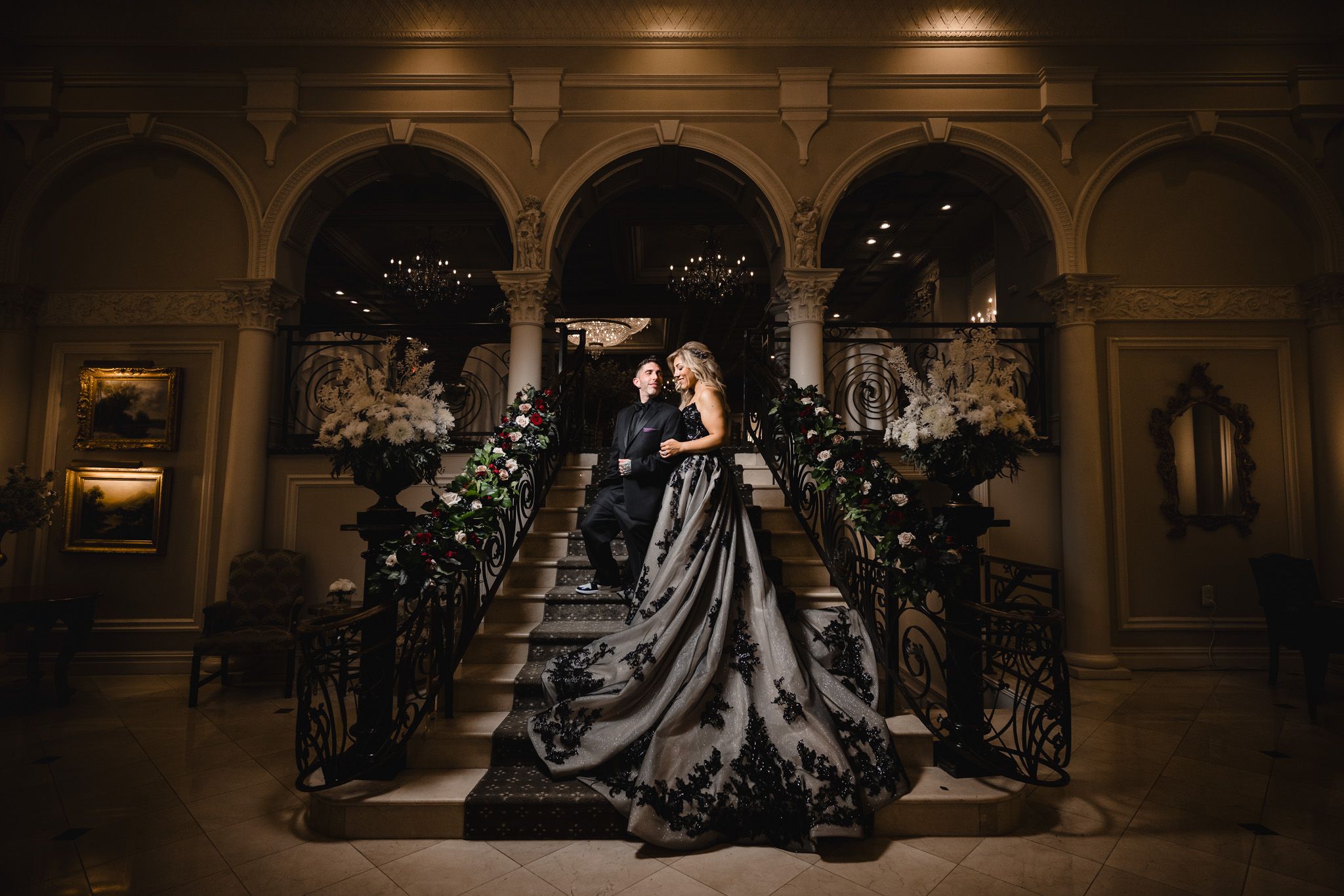 A dramatic wedding photo on an elegant staircase with arched architecture and twinkling lights.