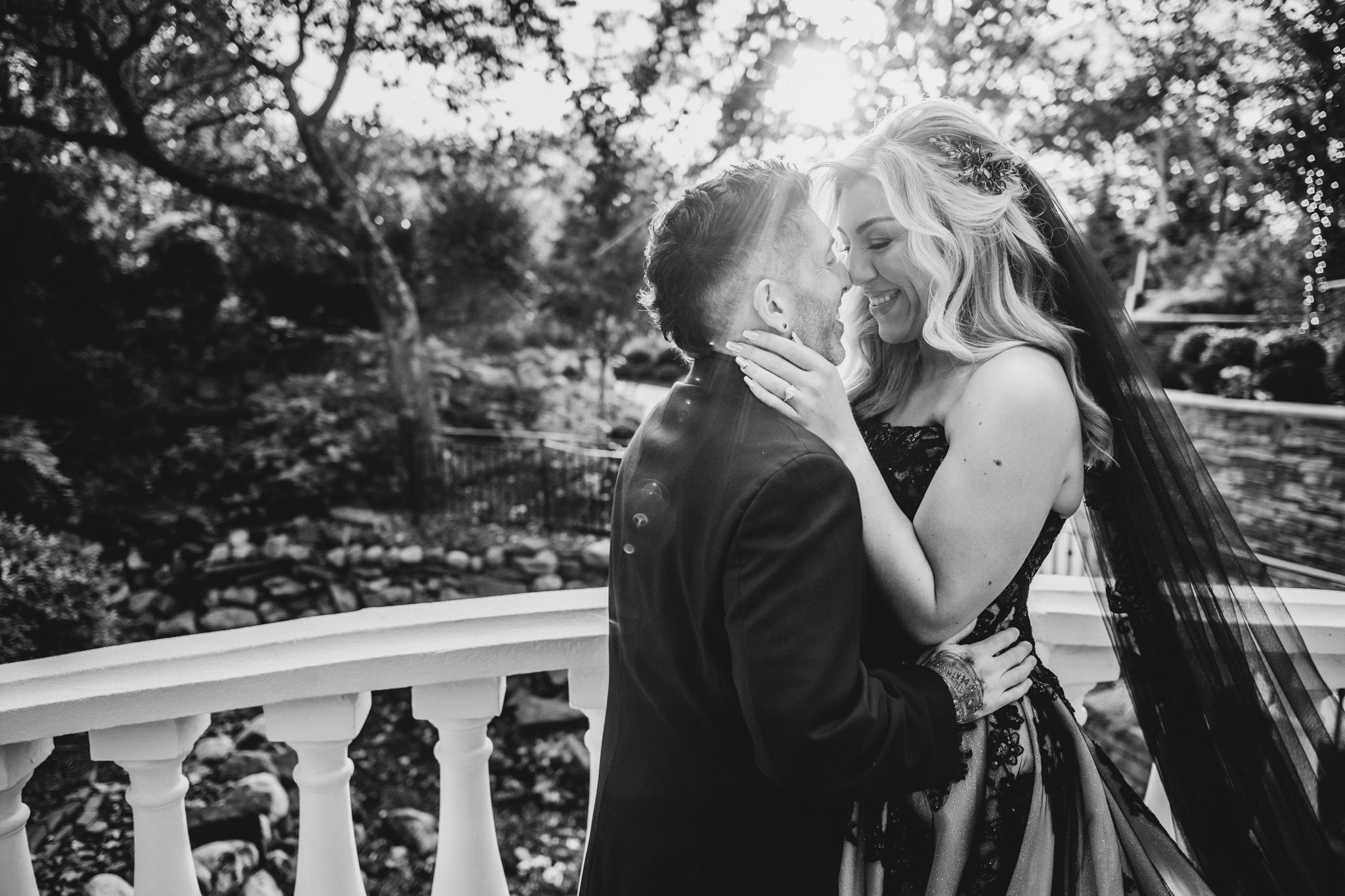 A couple shares a passionate kiss on an elegant white balcony in a garden setting.