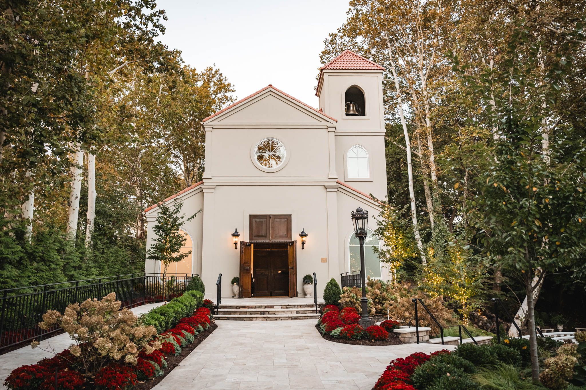 White chapel with bell tower and landscaped garden entrance on autumn day.