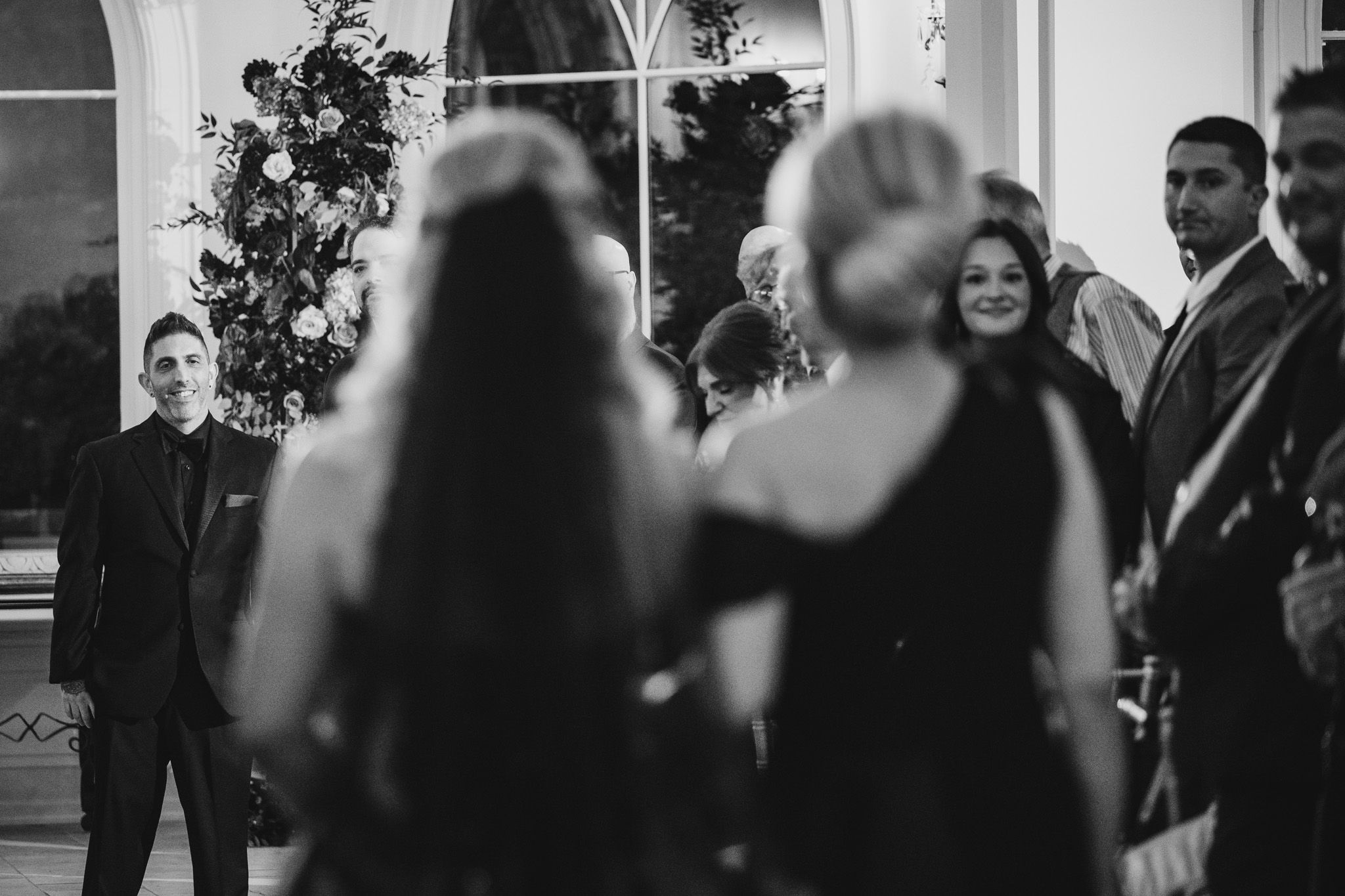 Black and white photo of wedding guests mingling in an elegant reception space with dramatic lighting.