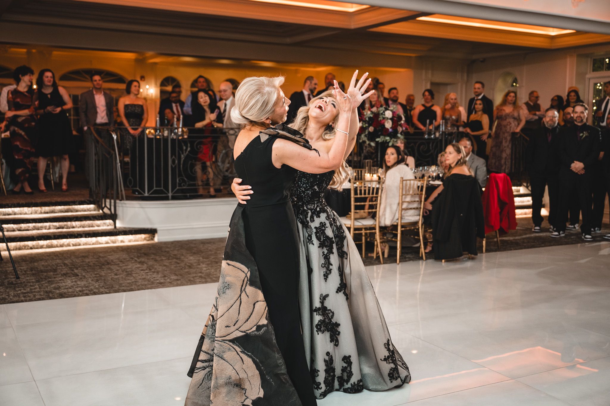 Wedding celebration in a grand ballroom with guests dancing and mingling.