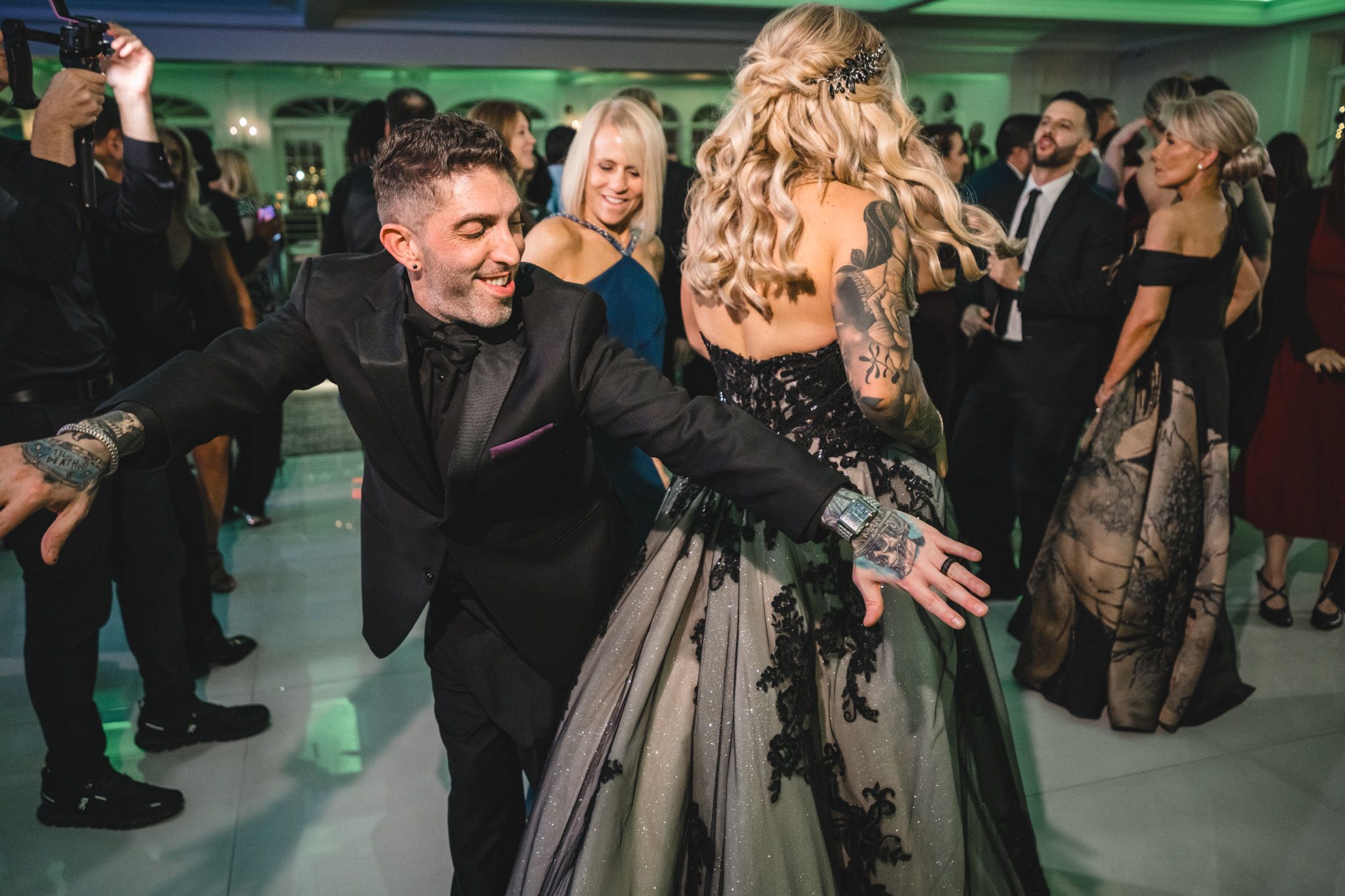 Wedding guests dancing under green mood lighting at an evening reception.