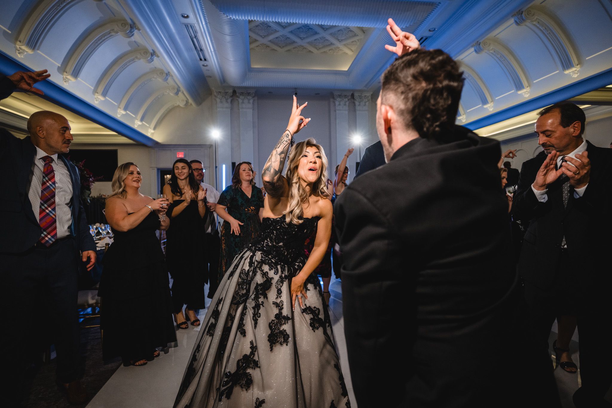 Wedding guests dance and celebrate on a dance floor illuminated by blue lighting in an elegant ballroom.