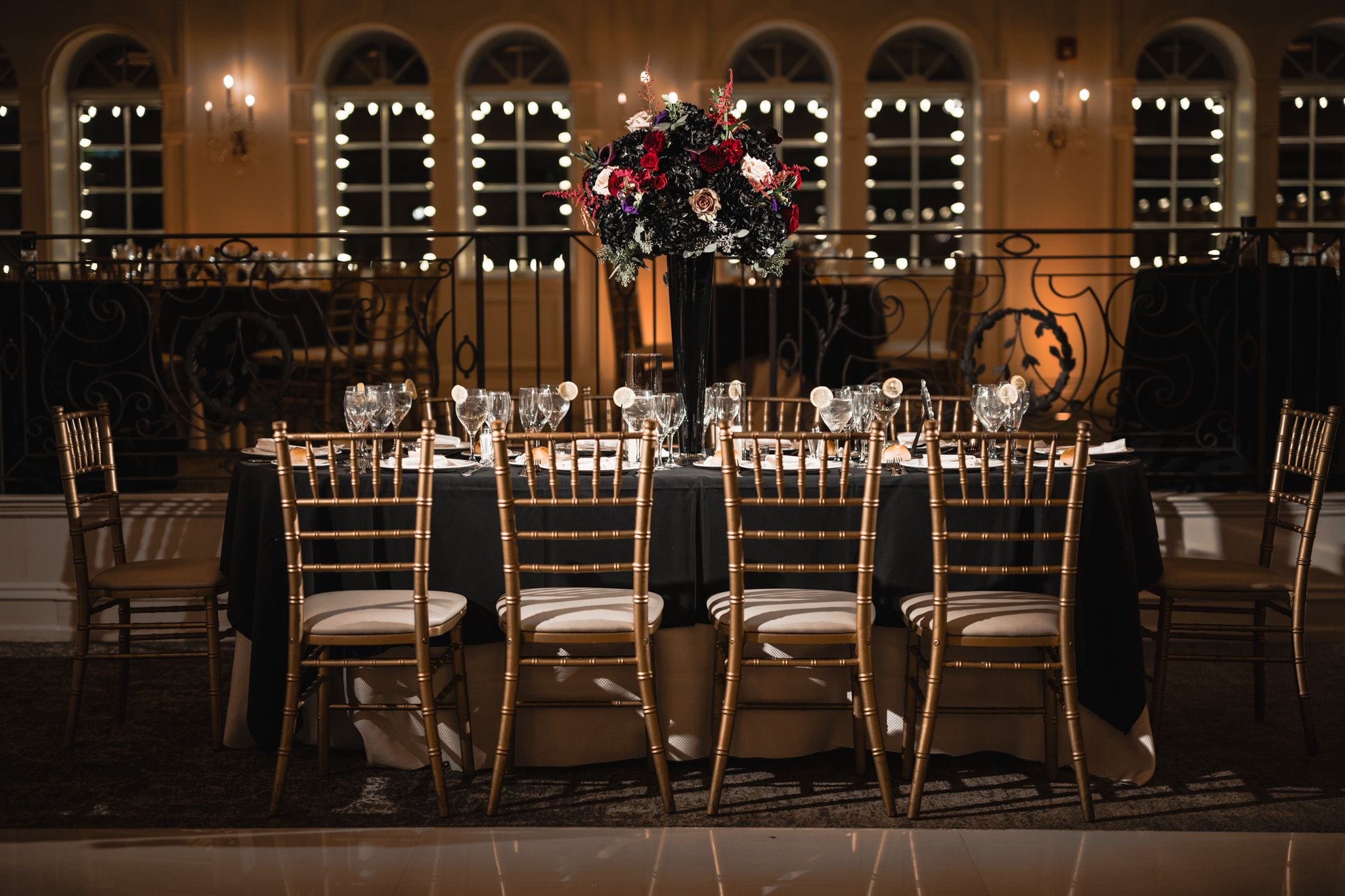 Elegant wedding reception table settings with gold chairs in a dimly lit ballroom.