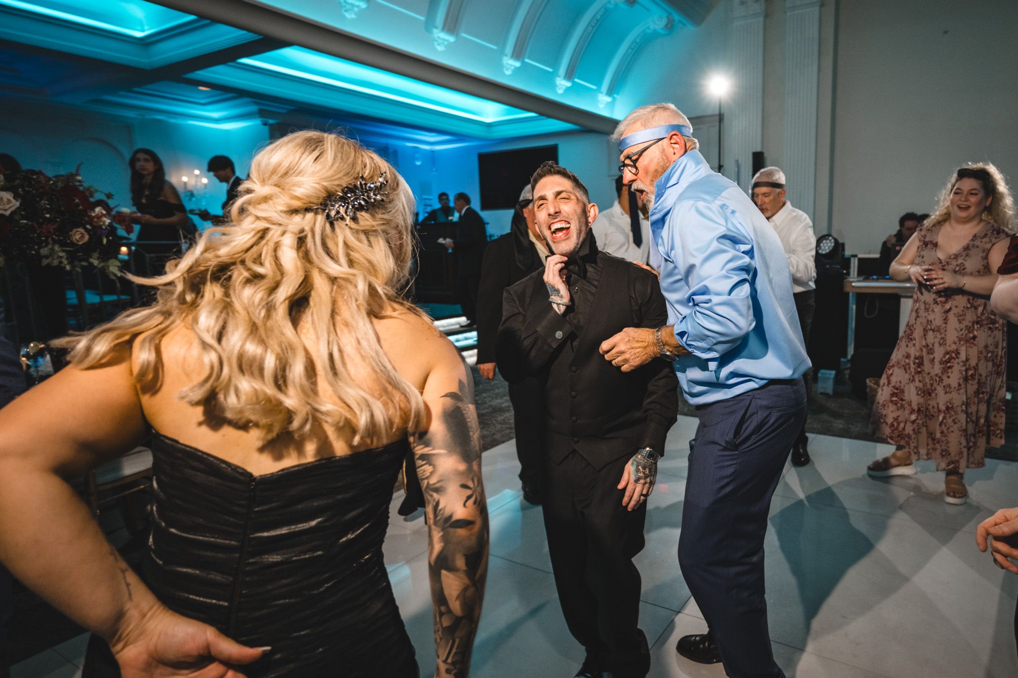 Party guests dancing under blue ambient lighting at an indoor celebration venue.