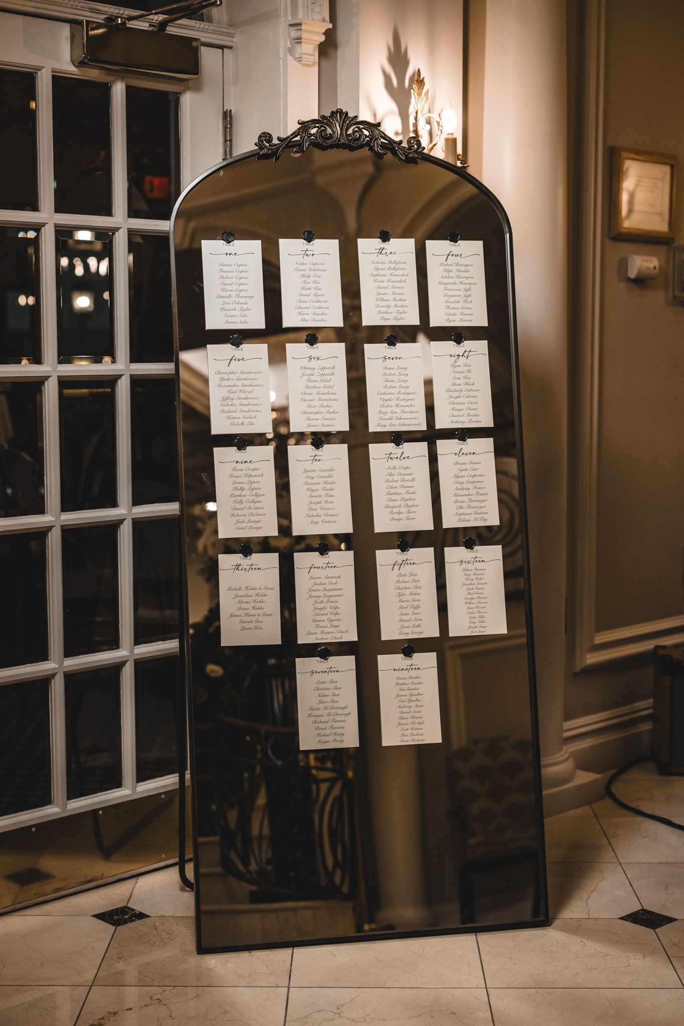 Seating chart display with handwritten cards on an ornate frame stand.