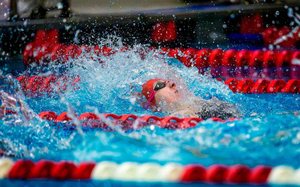 Cumberland Valley swimmer in red cap finishing a backstroke race, water splashing around, at the Keystone swim meet.