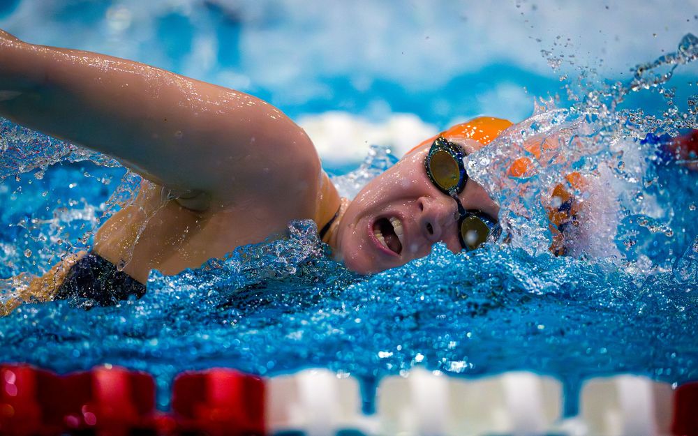 Hershey swimmer in orange cap smiling while swimming freestyle during the meet against Cumberland Valley.