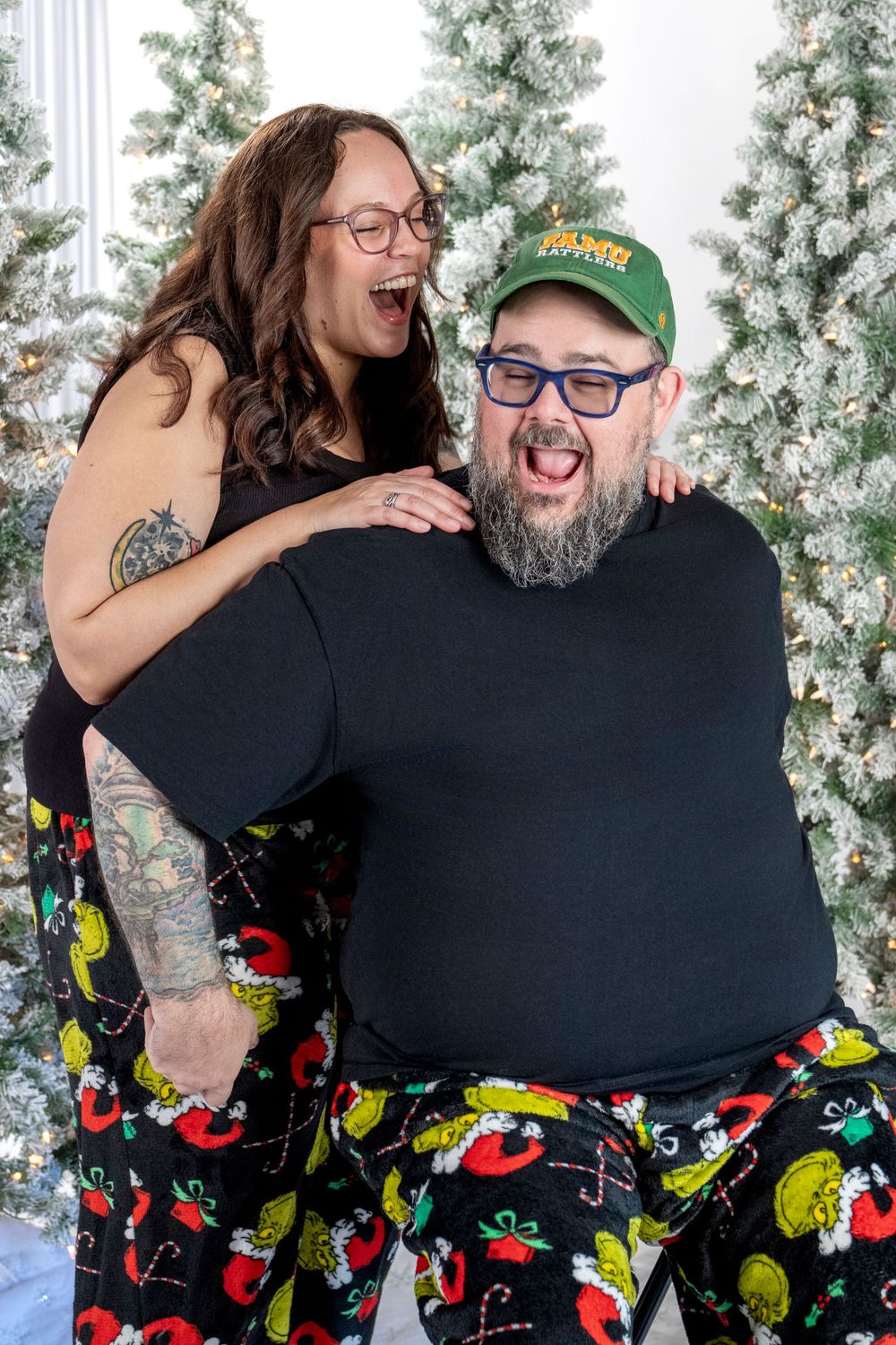 Two people share a joyful moment in front of a white Christmas tree wearing colorful patterned clothing.