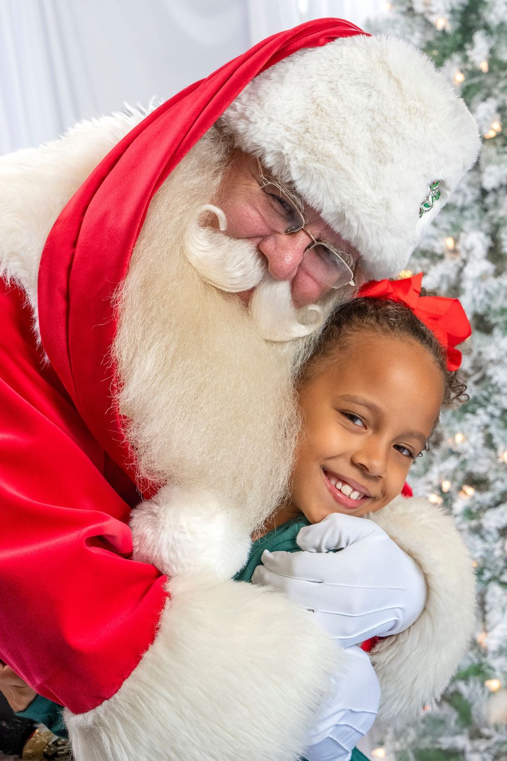 A child shares a heartwarming moment with Santa Claus against a snowy backdrop with twinkling lights.