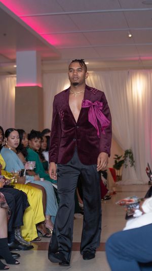 Purple velvet blazer with bow detail styled with black pants on fashion runway.