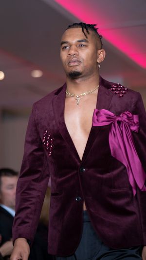 Purple velvet blazer with satin bow detail being presented on fashion show runway.