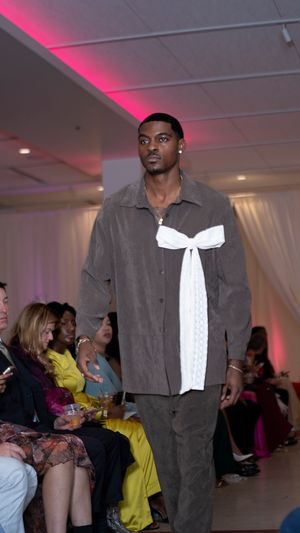 Grey suit jacket with white ruffled detail presented at evening fashion show.