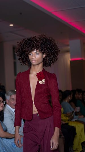 Burgundy velvet blazer with plunging neckline and brooch detail shown on fashion runway.