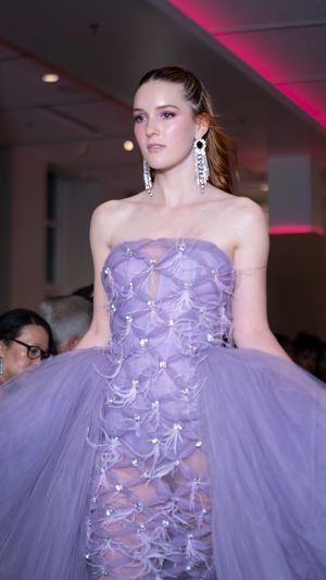 Model walks runway in ethereal lavender tulle gown with bow details and strapless neckline at fashion show.