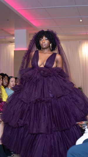 Model walks runway in dramatic deep purple ruffled tulle gown with voluminous tiered skirt at fashion show.
