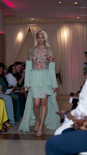 Model walks barefoot on runway wearing mint green high-low dress with embellished bodice at fashion show.