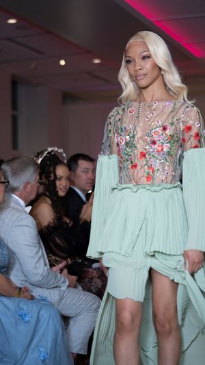 Model presents mint green dress with floral embellishments during fashion show.