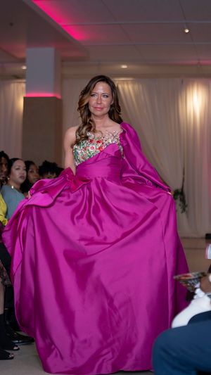 A model walks the runway in a flowing magenta ball gown during a fashion show presentation.