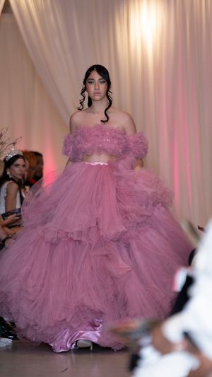 Dramatic pink tulle ballgown with ruffled layers flows across fashion runway stage.