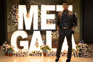 Models showcase a variety of black outfits on a fashion runway with floral decorations and illuminated letters in the background.