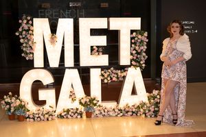 Fashion show stage setup with illuminated MET GALA signage and floral decorations.