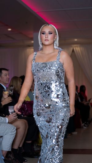 Sequined silver dress sparkles under runway lights at evening fashion show.