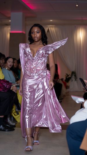 Metallic pink gown with dramatic architectural details being presented on fashion runway.
