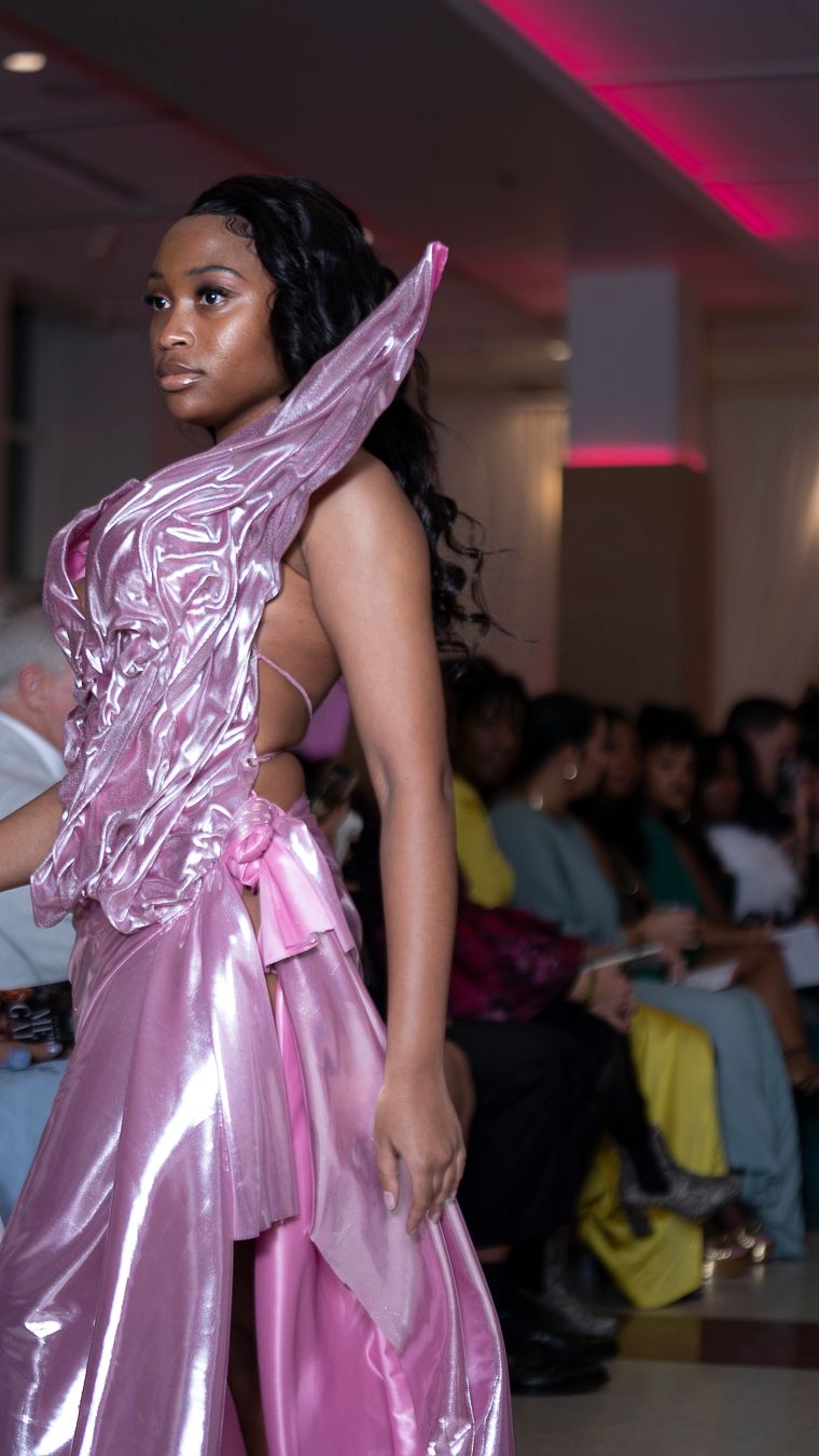 Models walk the runway in shimmering pink satin gowns during a fashion show with pink accent lighting.