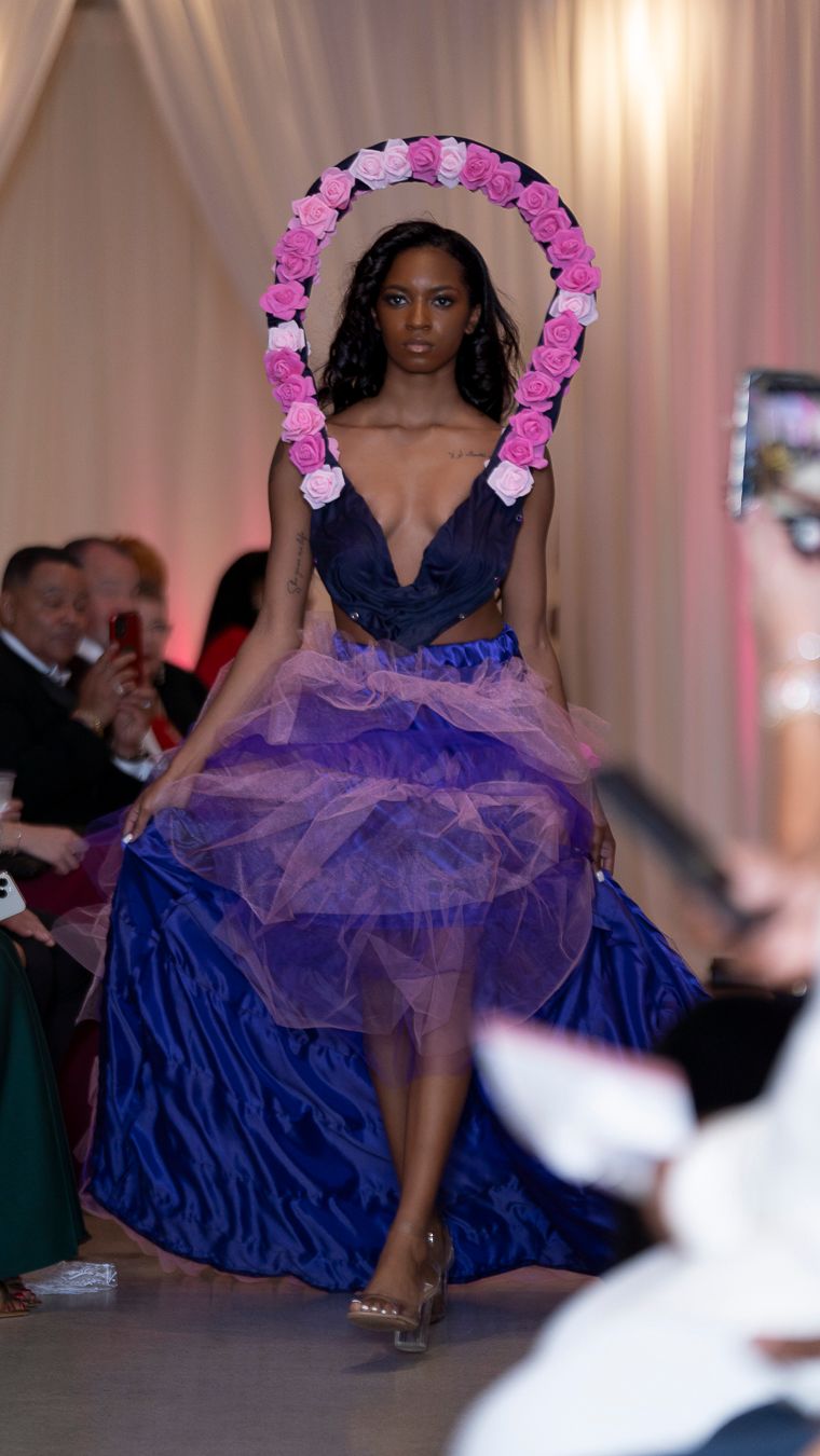 Navy blue ballgown with tulle skirt and pink floral crown shown on fashion runway.