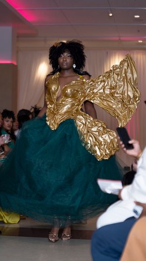 A dramatic evening gown featuring gold metallic details and dark teal tulle skirt displayed on a fashion runway.