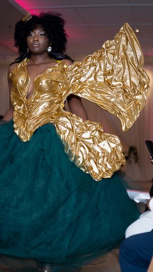 Model showcases stunning gold metallic top with dramatic sleeves paired with emerald green ballgown skirt on runway.
