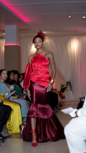 Deep red satin evening dress with dramatic silhouette shown on illuminated catwalk.