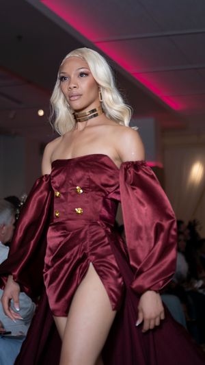 Burgundy satin mini dress with puff sleeves showcased on illuminated runway.