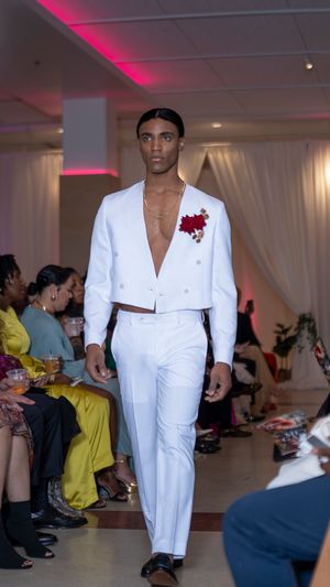 Crisp white suit ensemble with red flower accent presented at fashion show.