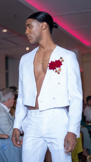 Crisp white suit with red floral accent shown on fashion runway.