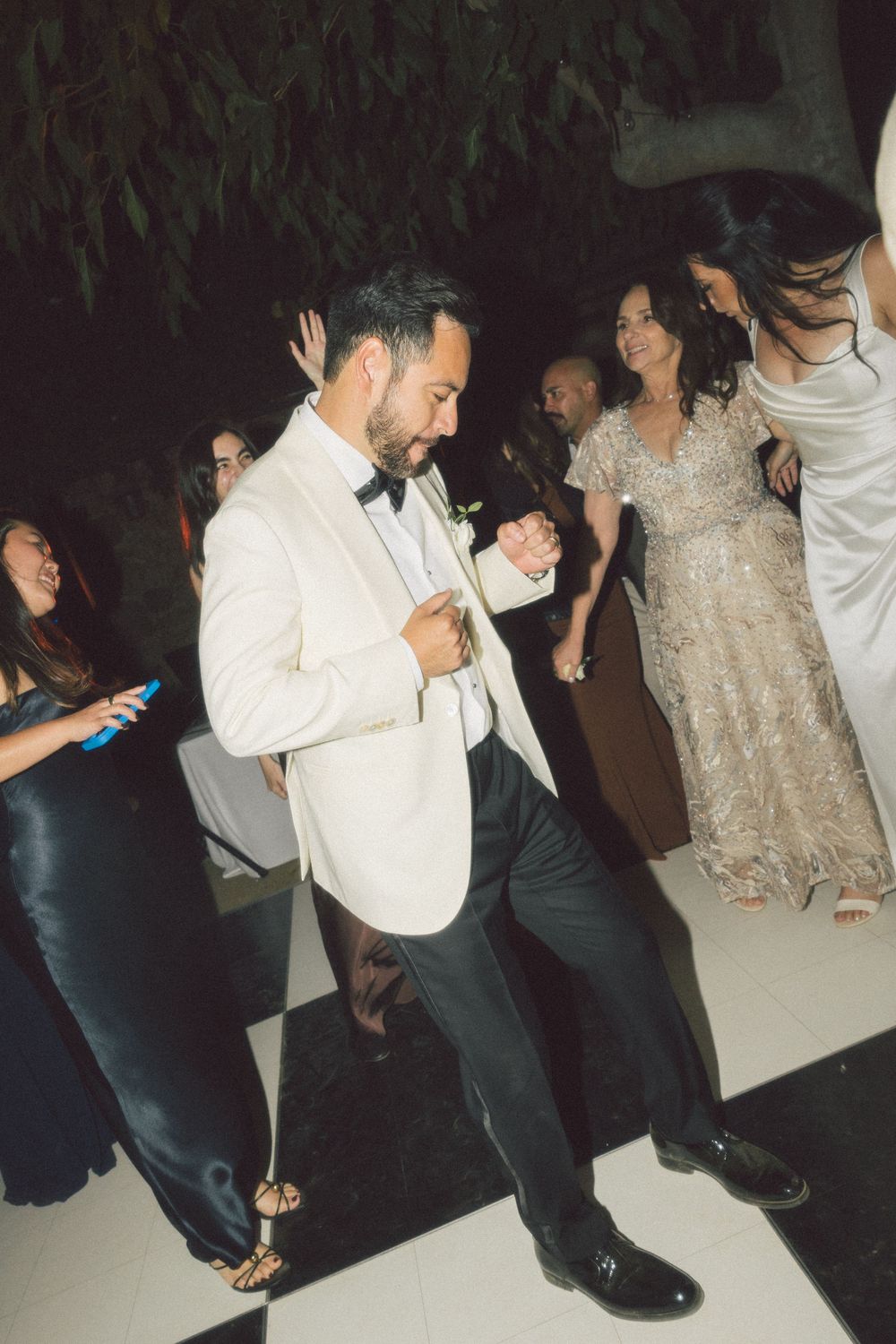 People dancing and enjoying themselves at a party or celebration with dark lighting and formal attire.