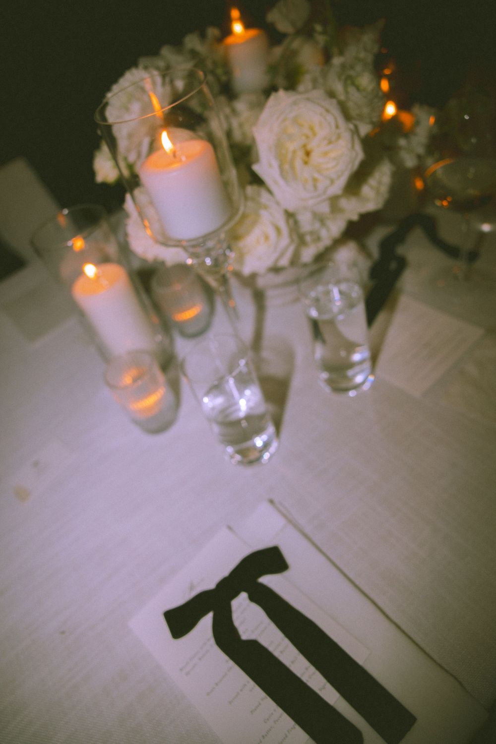 Romantic table setting with glowing candles, white roses, and wine glasses creating an intimate ambiance.