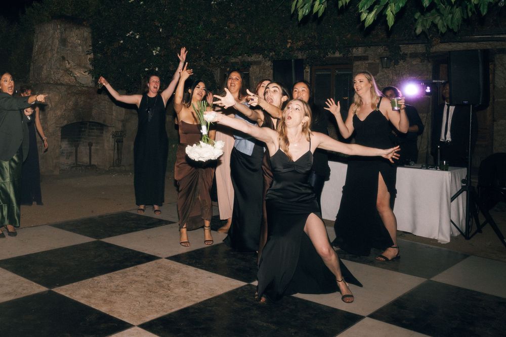 Wedding guests dance together on a dark dance floor during an evening reception celebration.
