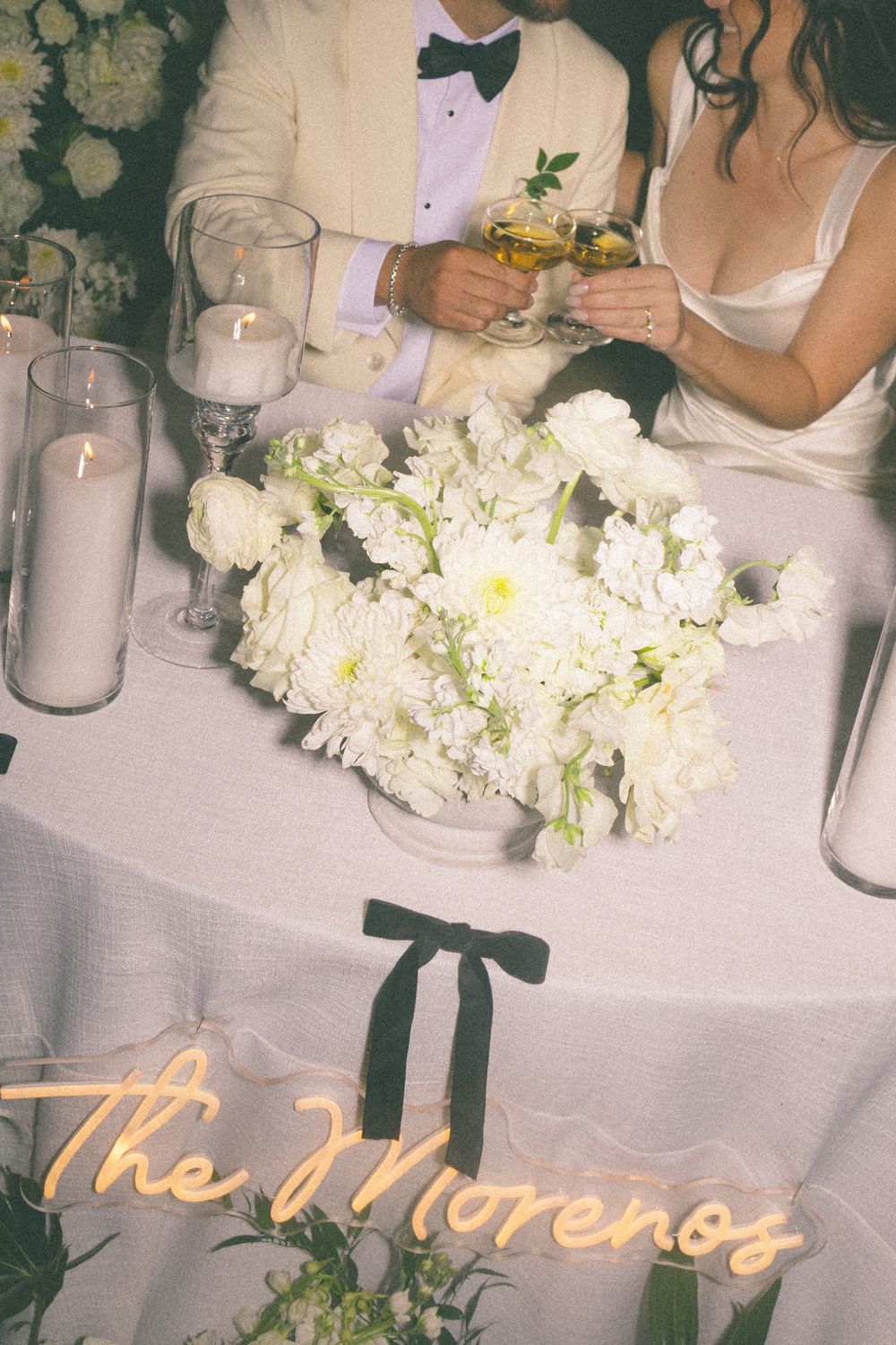 Elegant wedding reception table decorated with white floral arrangements, candles and gold script name cards.