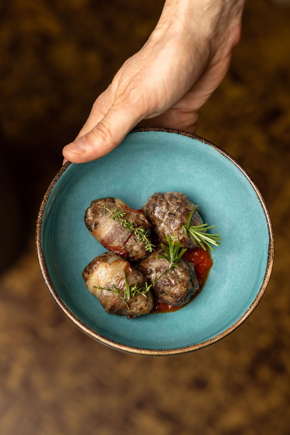 Small roasted potatoes garnished with fresh herbs and tomato served in a turquoise ceramic bowl.