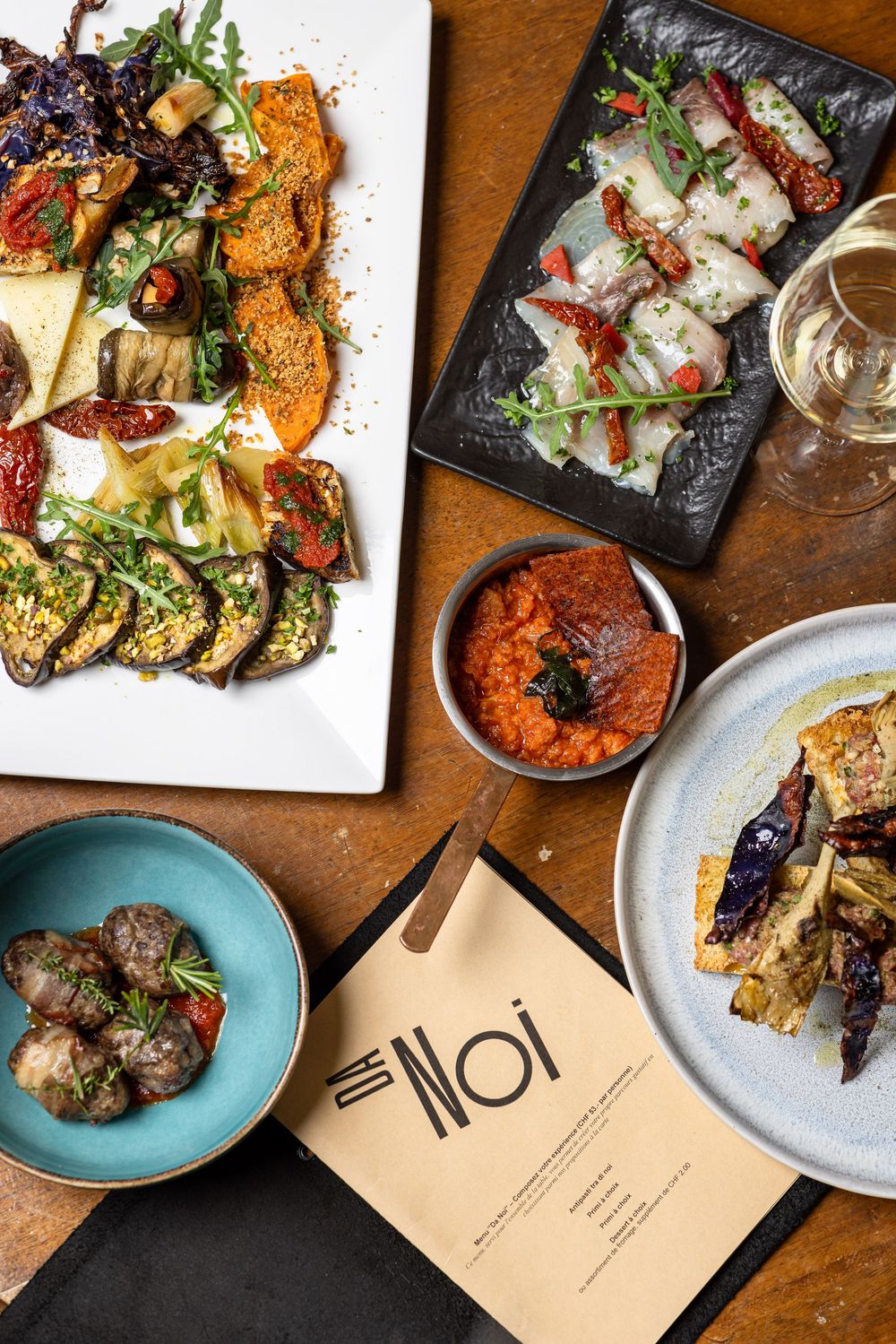 Overhead view of elegant restaurant dishes including grilled vegetables, meatballs and menu on wooden table.